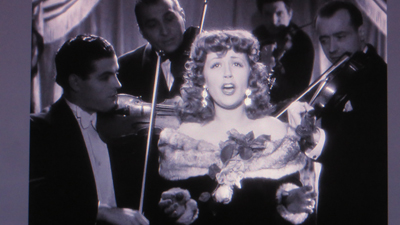 The image of four violinists playing around a night club singer is inspired by a scene of Suzy Delair singing Dance Avec Moi in the 1947 noir crime film Quai des Orfèvres, directed by Henri-George Clouzot, sometimes known as The French Hitchcock. Quai des Orfèvres is the location of the Paris Police headquarters